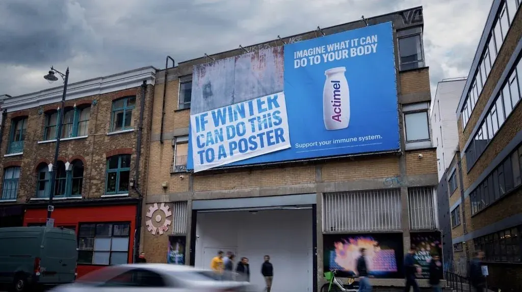 Urban street scene with a large Actimel advertisement on a blue billboard