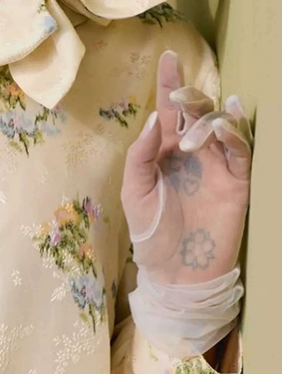 Portrait of a person with a wrapped, tattooed hand held to their chest, wearing a floral dress and hat Portrait of a person with a wrapped, tattooed hand held to their chest, wearing a floral dress and hat