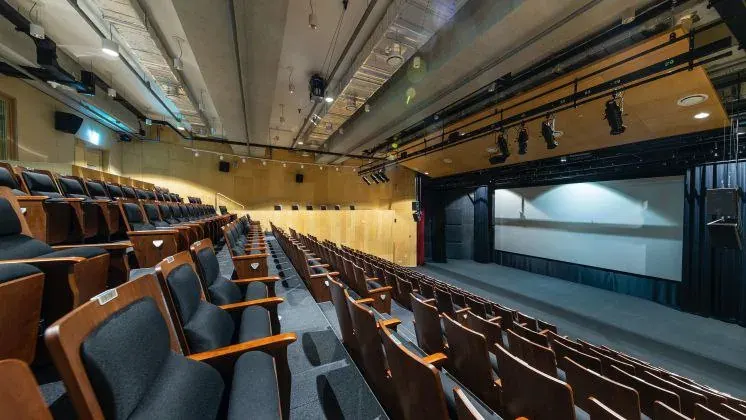 Empty auditorium with rows of seats facing a stage and large screen, suggesting preparation for a mobile game launch presentation Empty auditorium with rows of seats facing a stage and large screen, suggesting preparation for a mobile game launch presentation