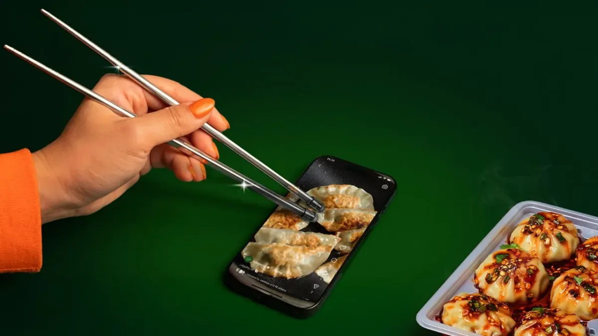Hand using chopsticks to tap dumpling icons on a smartphone next to a tray of dumplings, suggesting careful selection like choosing a UA agency Hand using chopsticks to tap dumpling icons on a smartphone next to a tray of dumplings, suggesting careful selection like choosing a UA agency