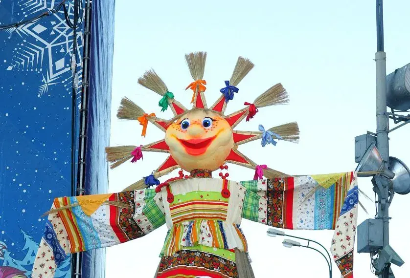 Colorful scarecrow-like figure with a round smiling sun head and patchwork clothing on a street setup